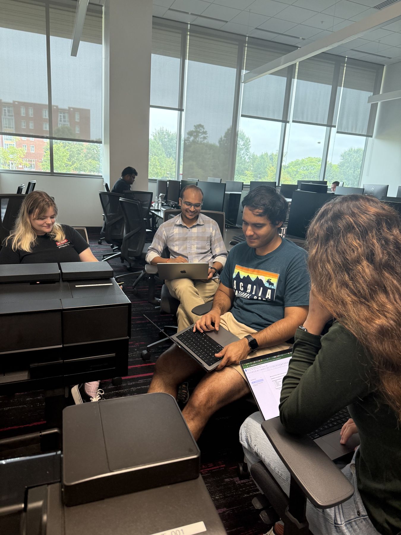 Four participants gather around their laptops to work through a problem together at the 2025 NC State hackathon